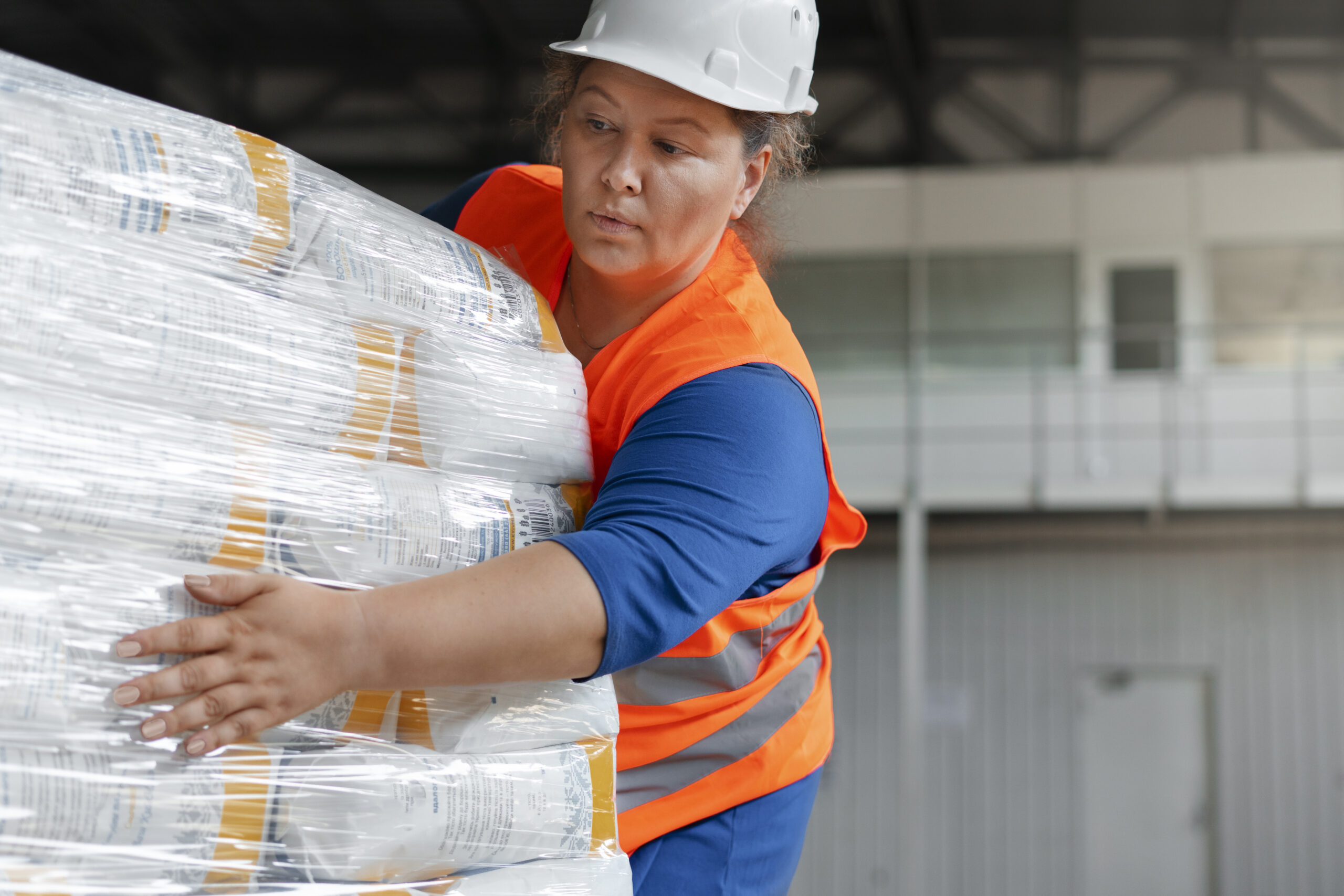 Warehouse worker in safety vest handling shrink-wrapped freight pallet at loading dock